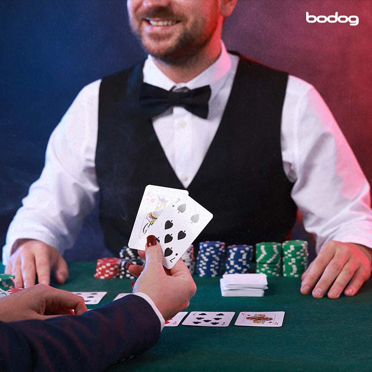 jugador sosteniendo 2 cartas en frente a crupier en mesa de casino